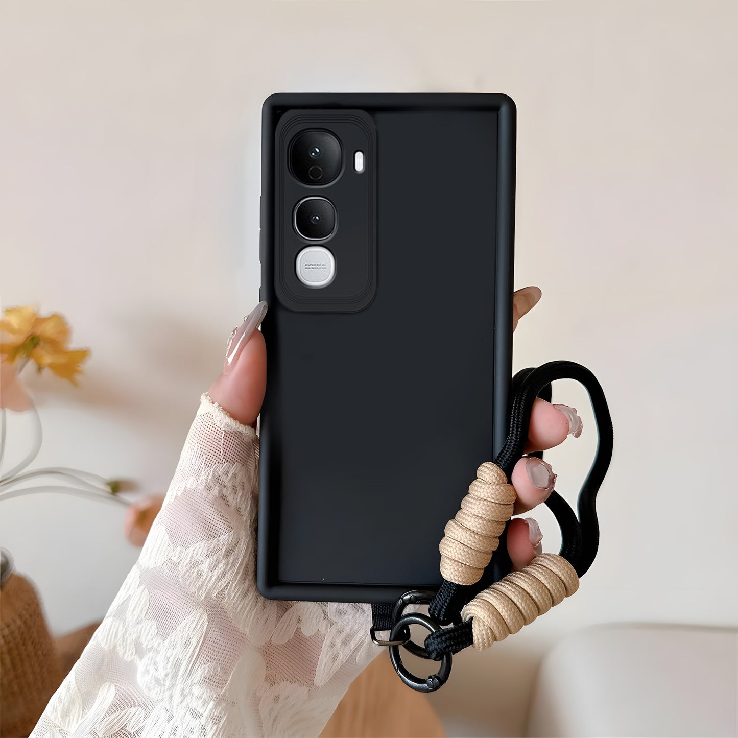 Black phone case with a beige cord held by a hand against a neutral background